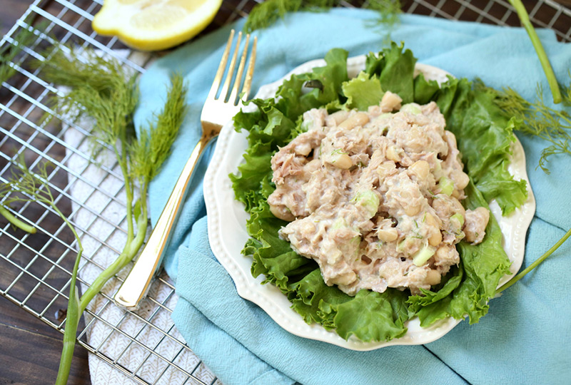 Light tuna salad on a bed of greens served on a small white plate. 