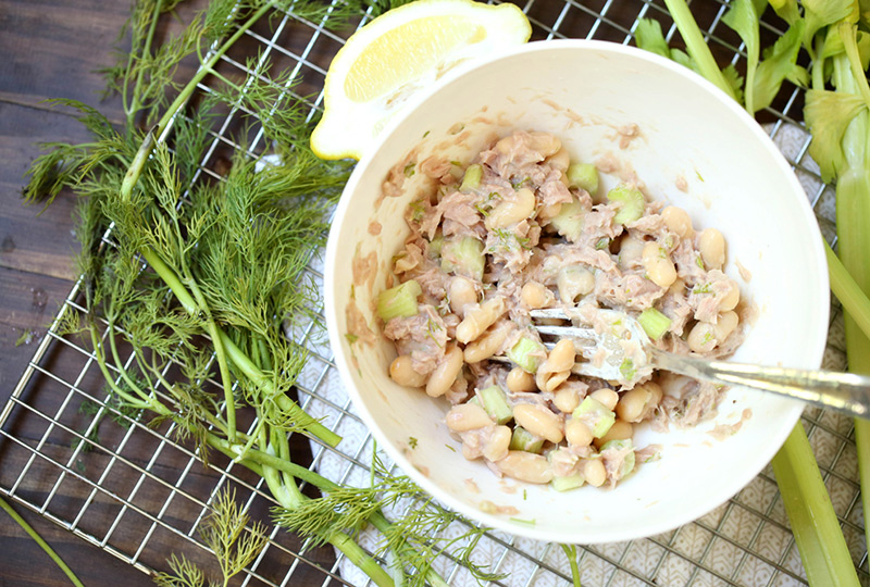 Tuna being mixed with cannellini and celery in a bowl. 