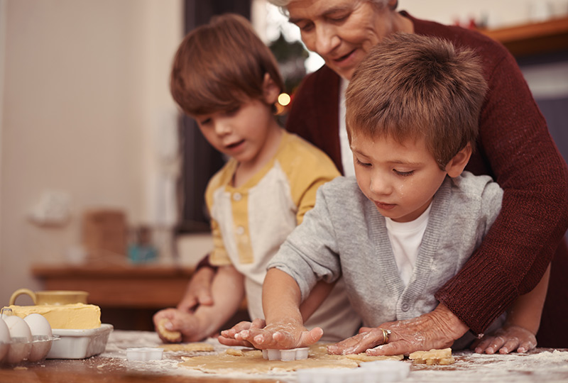 Two young boys baking cookies with their grandmother