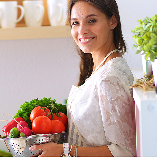 Woman in a white lace dress holds a bowl of bright red tomatoes