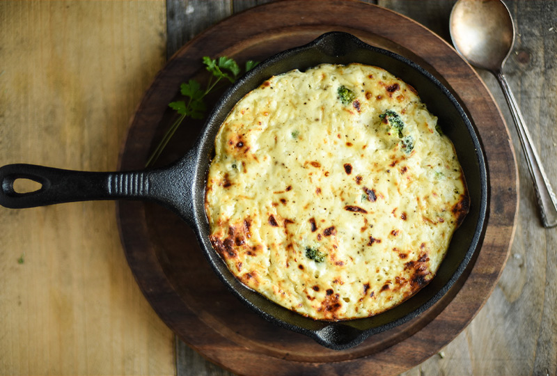 Cast iron pan containing baked broccoli-cheese casserole