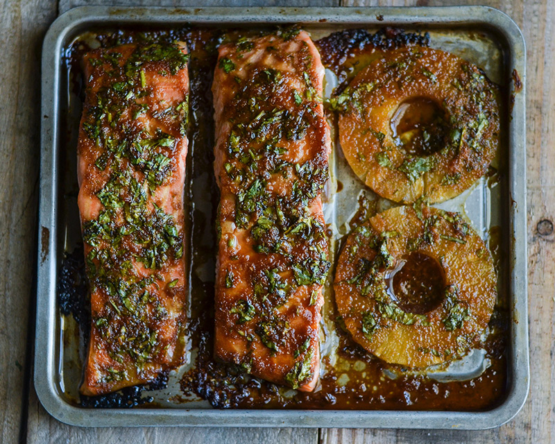 Two salmon fillets and pineapple rings baked on a sheet pan