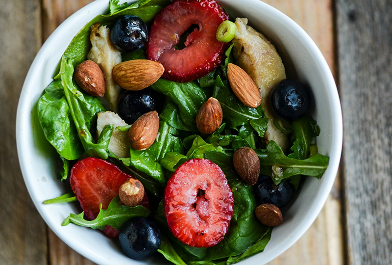 White salad bowl containing salad of leafy greens, berries and chicken