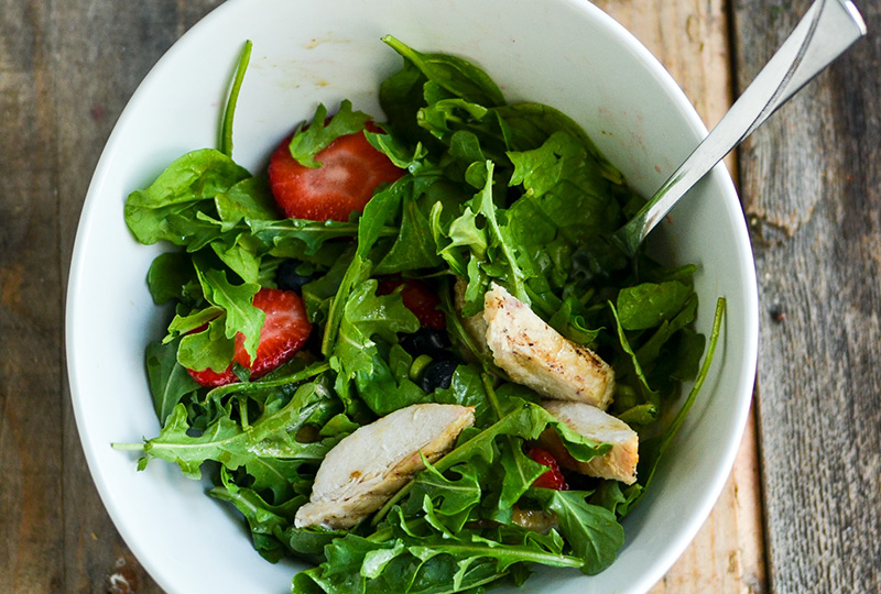 Leafy green salad, chicken and berries in a bowl, tossed with dressing.