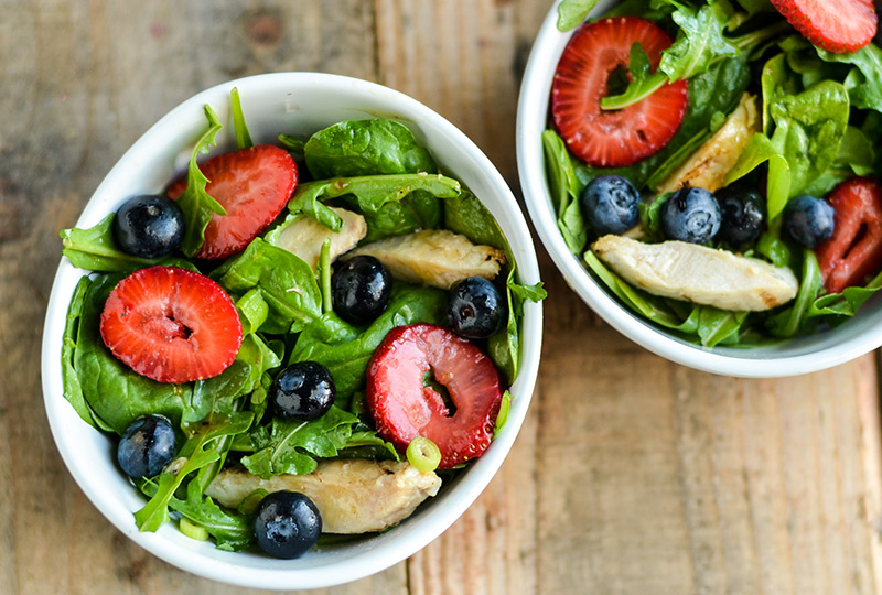 Two bowls with salads of leafy greens, berries and chicken