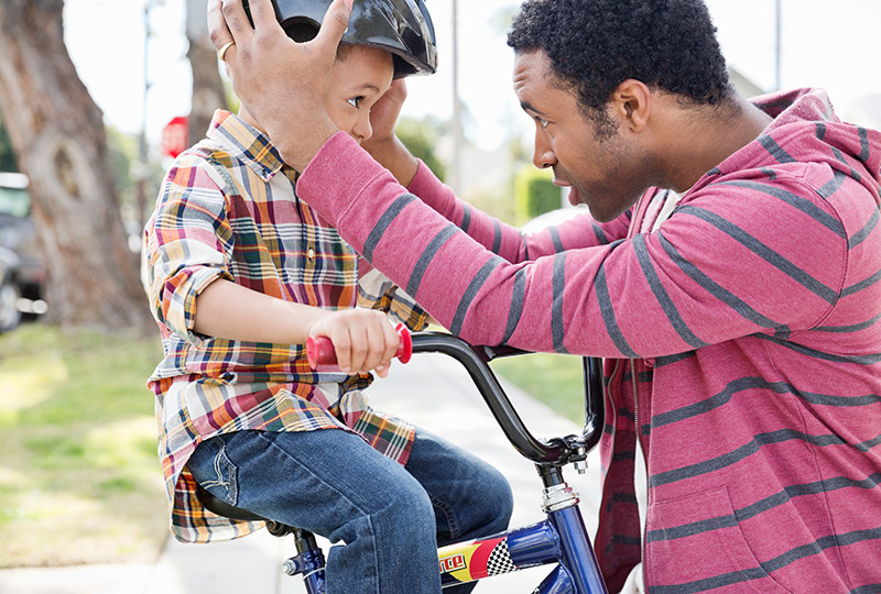 A father helps young son put on a bike helmet