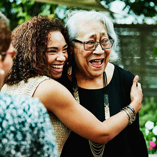 A young woman hugs an older woman in a backyard full of people.