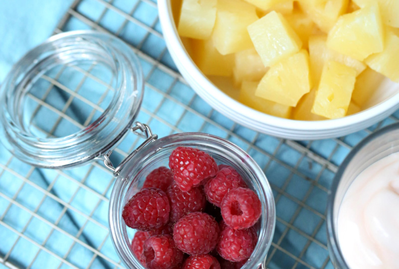 A bowl of pineapple chunks, a bowl of raspberries and a bowl of yogurt, ready to make parfaits.
