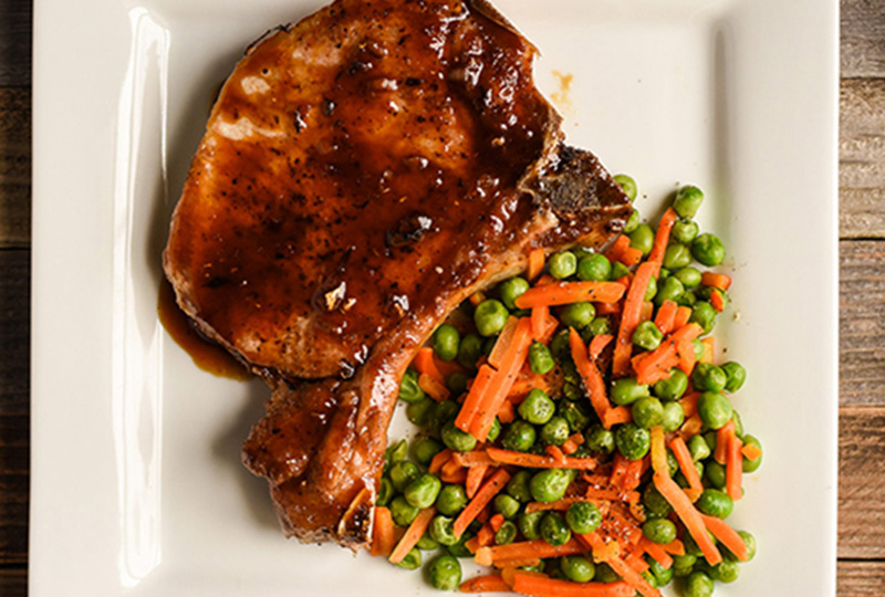 Pork chop glazed in orange-soy sauce, plated with cooked peas and carrots
