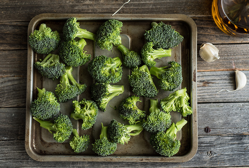 Raw broccoli florets spread on a baking sheet.