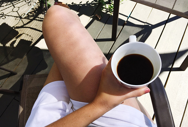 Overhead view of a woman holding a mug of black coffee on her lap