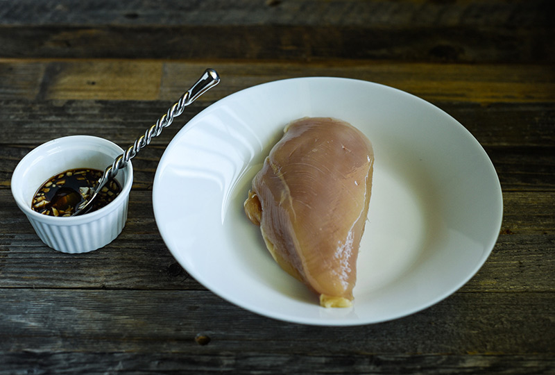 Raw skinless boneless chicken breast and a bowl of balsamic-honey-garlic marinade