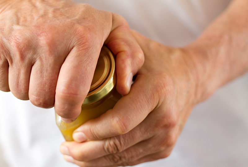 Closeup of a white man's hands as he works to open a jar