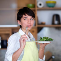 Woman eating a healthy plate of salad greens with sarcastic expression on her face.