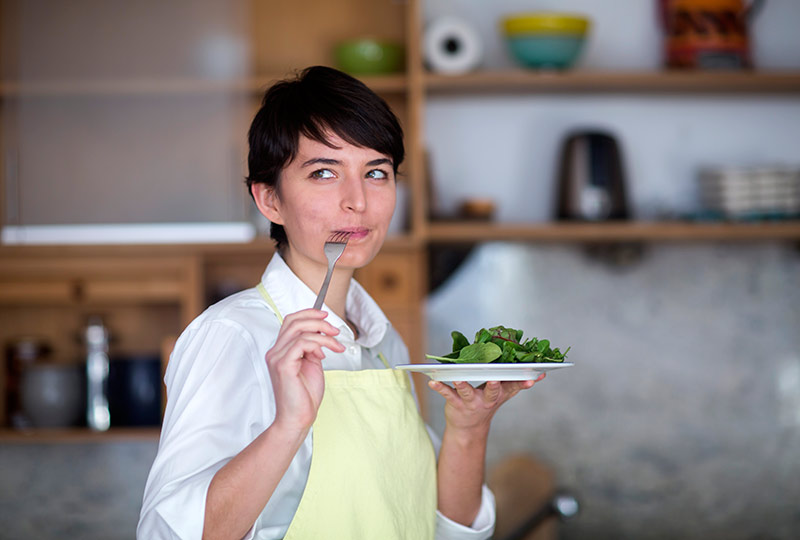 Woman eating a plate of salad greens with sarcastic expression on her face.