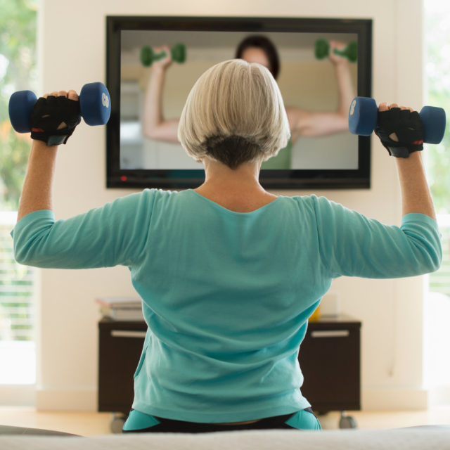 Women lifting weights and watching fitness video at home.