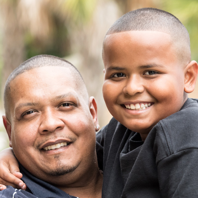 Father and young son at risk of obesity smiling at camera
