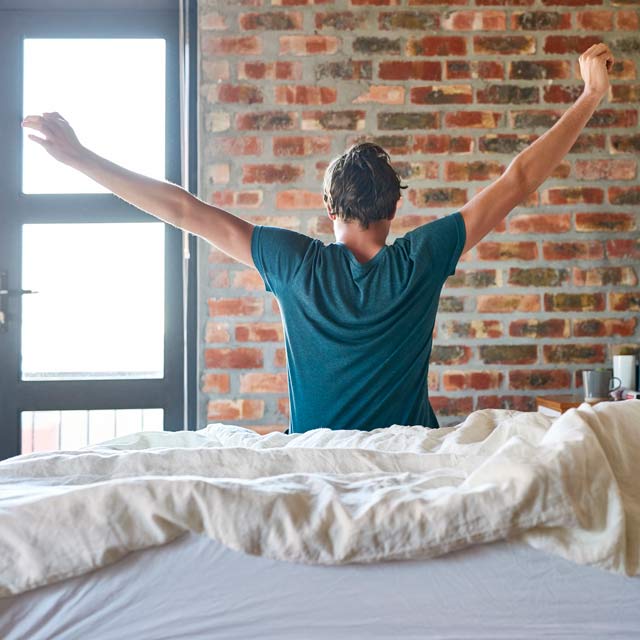 Adult rising from bed and stretching to prevent back pain