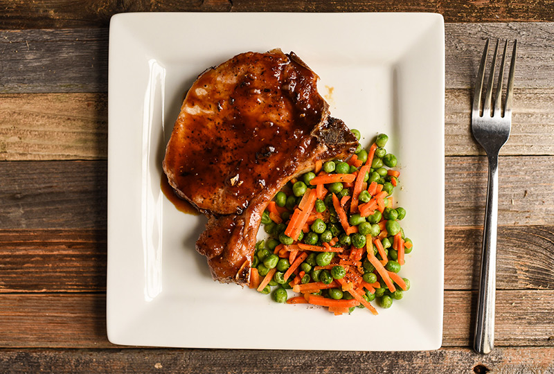Orange soy sauce pork chop with side of peas and carrots.
