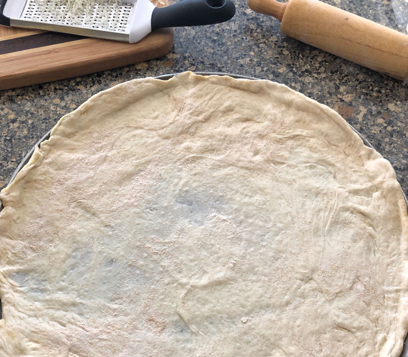 Raw pizza dough rolled out thin on a round pizza pan.
