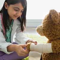A young girl wraps a bandage around a teddy bear's arm.