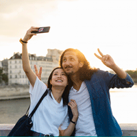 A woman takes a selfie of herself and a man standing on a bridge.