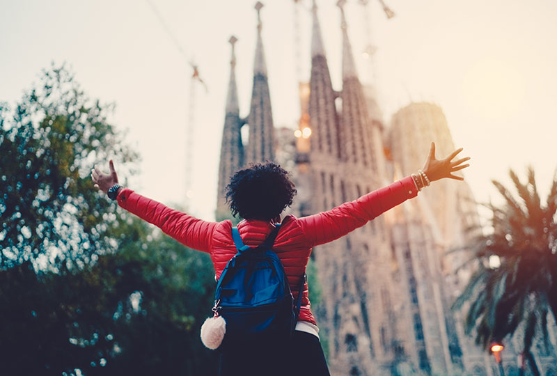 Following healthy travel tips can lead to happy travel experience like this woman posing in front of a cathedral in Spain.