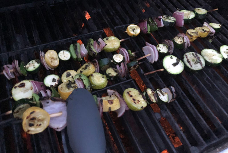 Skewered vegetables cooking on a grill.