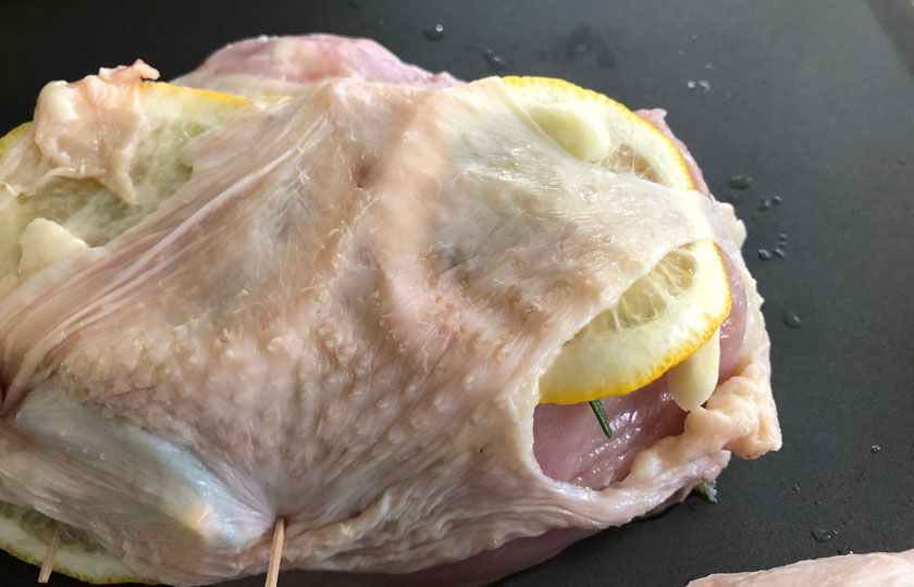 Closeup of raw chicken breast prepared with lemon slices and garlic, ready to grill. 