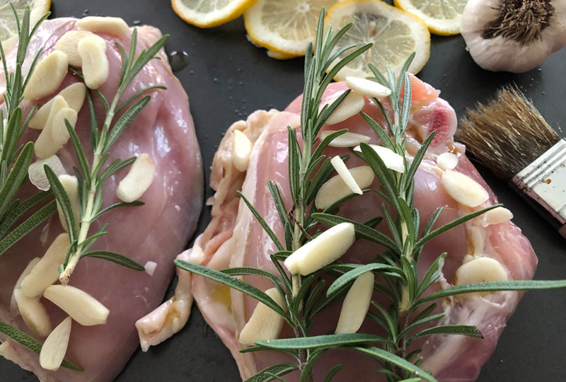 Closeup of raw chicken breast, covered with garlic cloves and rosemary sprigs