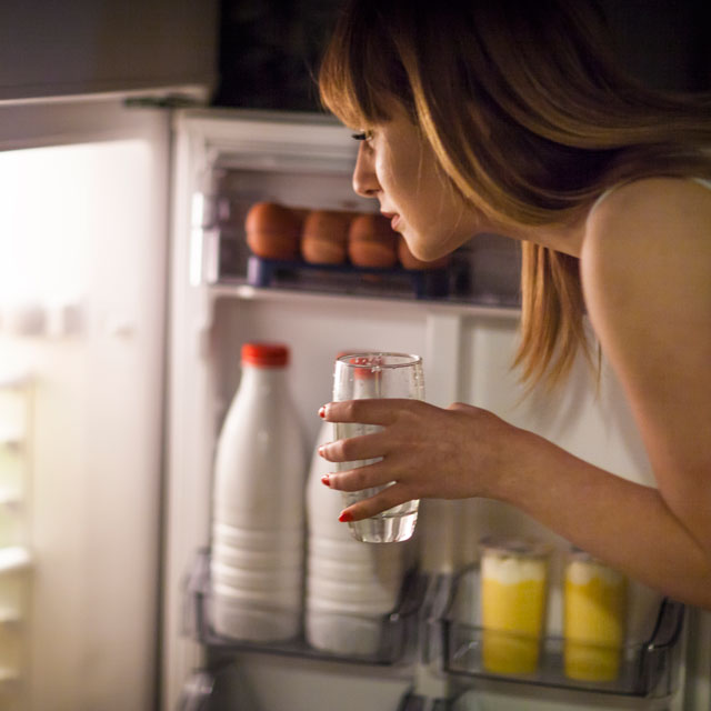 Woman looking into fridge looking for better alternatives to stop snacking at night.