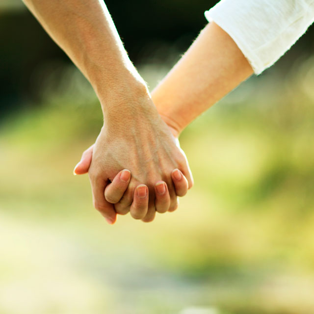Closeup of hands, a man and woman clasping hands outdoors.