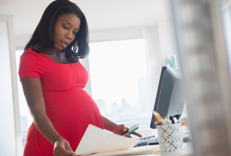 Pregnant African American woman stands at a work desk with computer