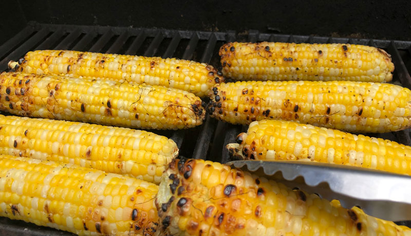 Closeup of ears of yellow corn cooking on a grill.