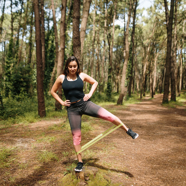 Woman working out in a forest with resistance bands around her legs.