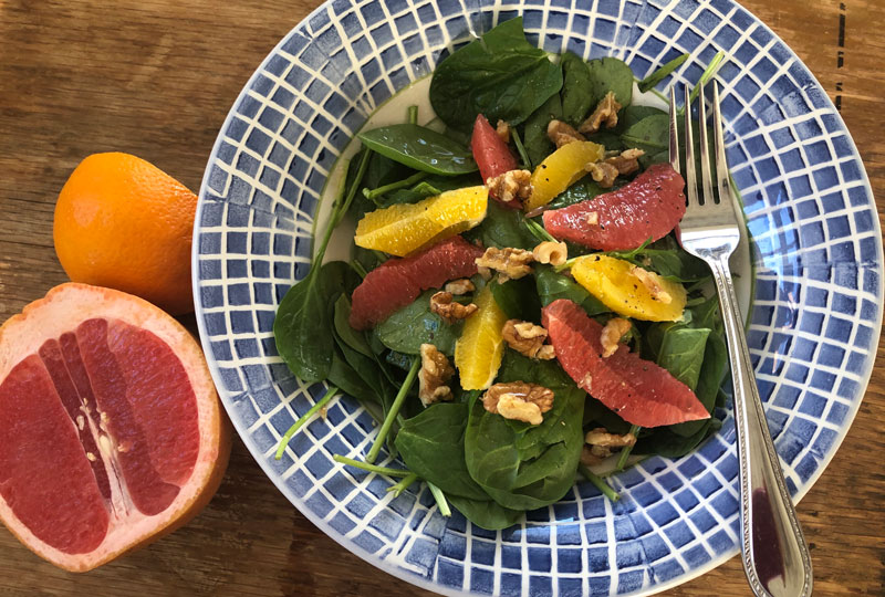 A salad of baby spinach and citrus wedges in a blue and white bowl.