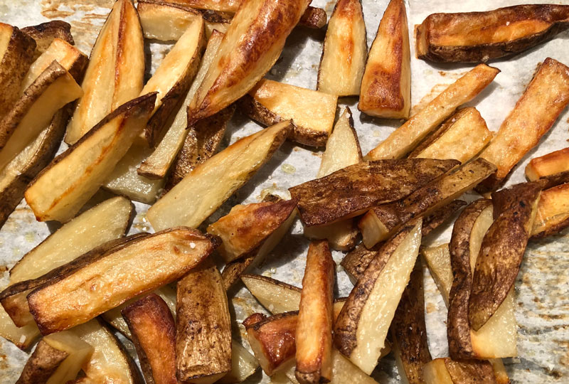 Closeup of baked potato fries on a sheet pan, just out of the oven.