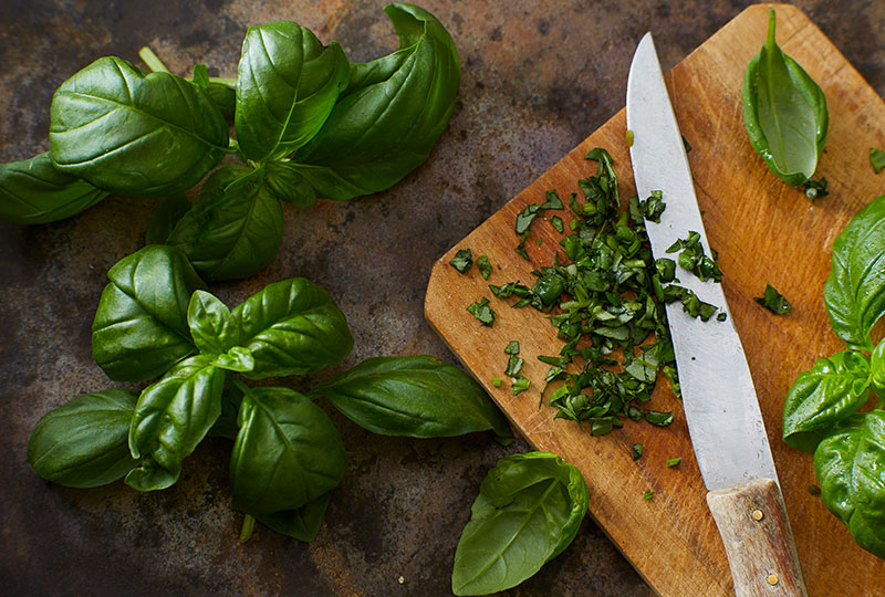 Fresh basil on a wood cutting board, some of it chopped small.