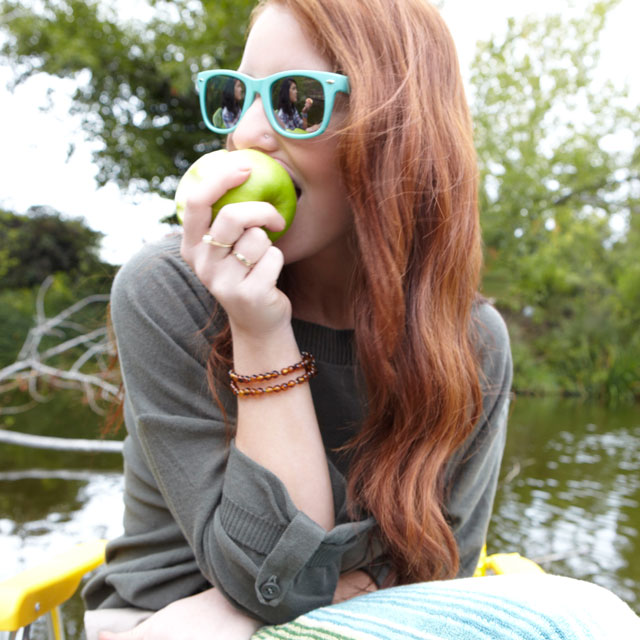 Young woman eats a green apple while sitting outdoors.