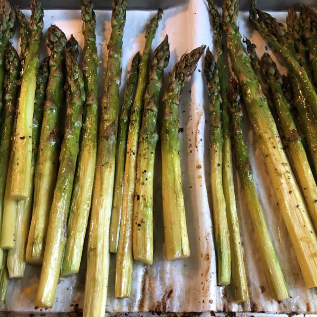 Roasted asparagus spears on a foil-lined baking sheet.