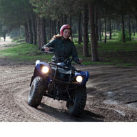 A teen girl drives an ATV through a dirt road in the forest while wearing a helmet.