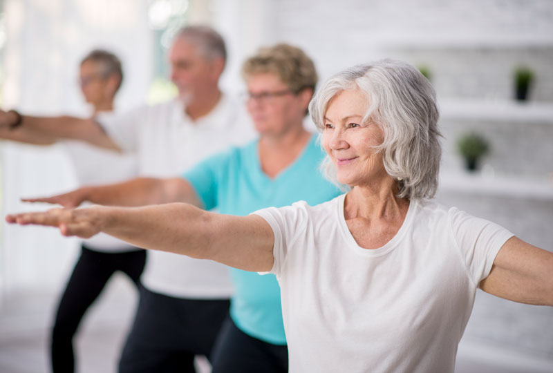 A group of older adults hold warrior pose in a yoga class.