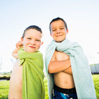 Two young boys pose while wrapped in swim towels on a summer day.