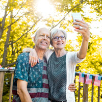 A middle-aged couple take a selfie standing outdoors on a deck in autumn.