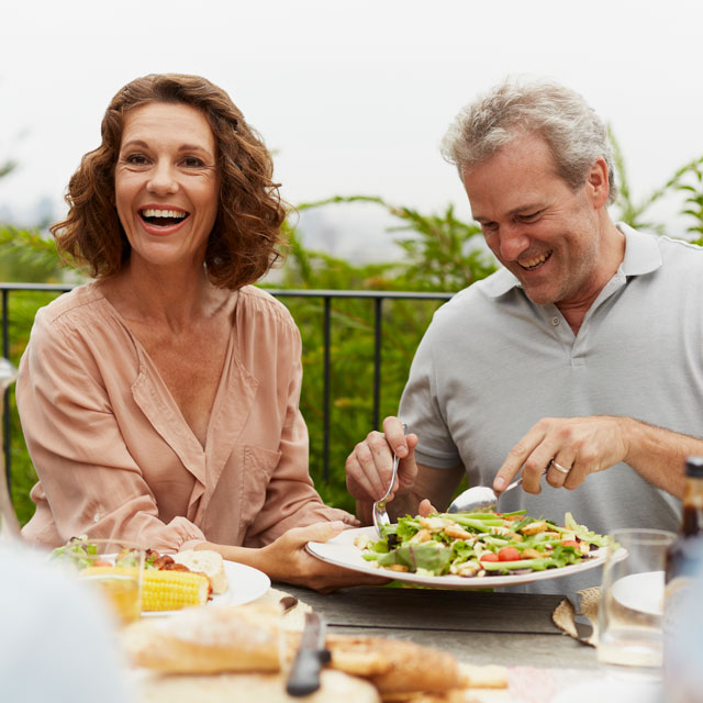A middle-aged white couple eat a light meal outdoors.