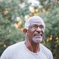 Closeup of middle-aged Black man wearing earbuds, walking outdoors.