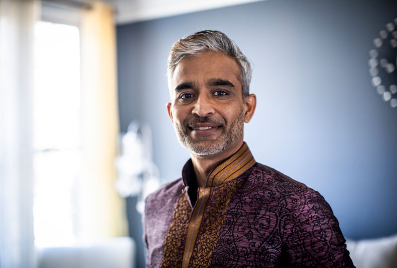 Head-and-shoulders portrait of a middle-aged Indian man standing indoors.