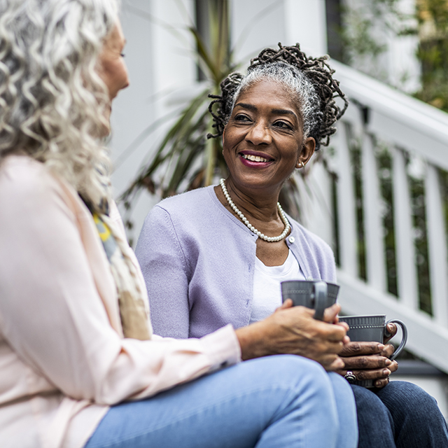 Two middle aged African American women sit on a stoop talking.