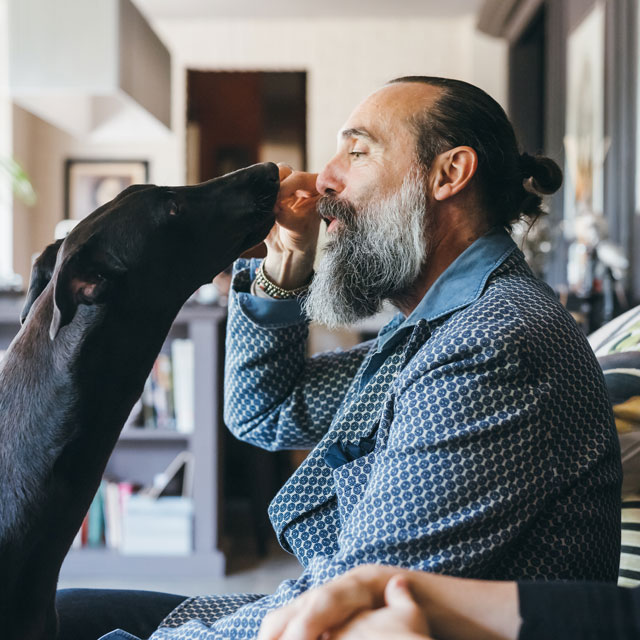 A middle aged man feeds his black lab dog a treat.