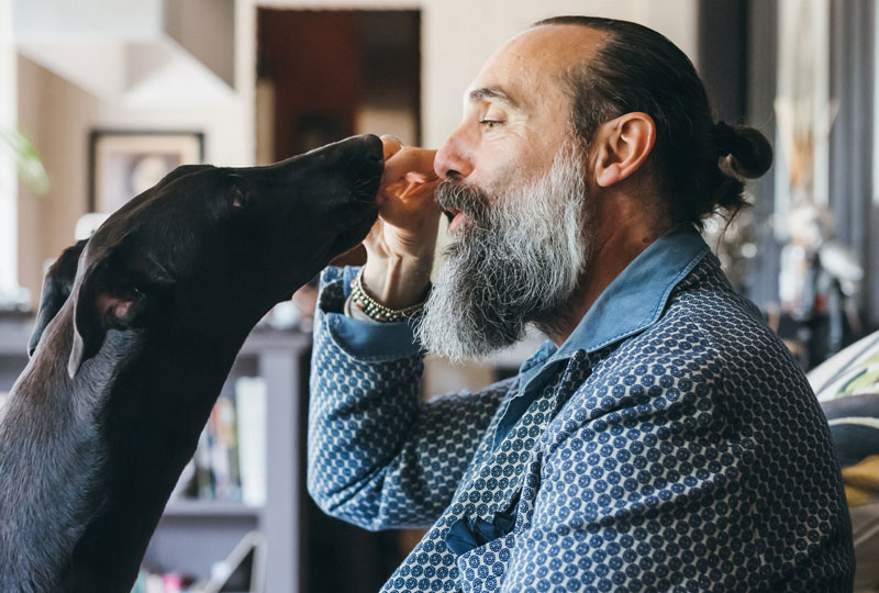 A middle aged man feeds his black lab dog a treat.